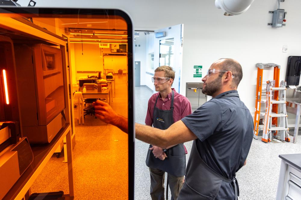 Tech Foundry at UC Davis Aggie Square employees stand near orange 3D printers